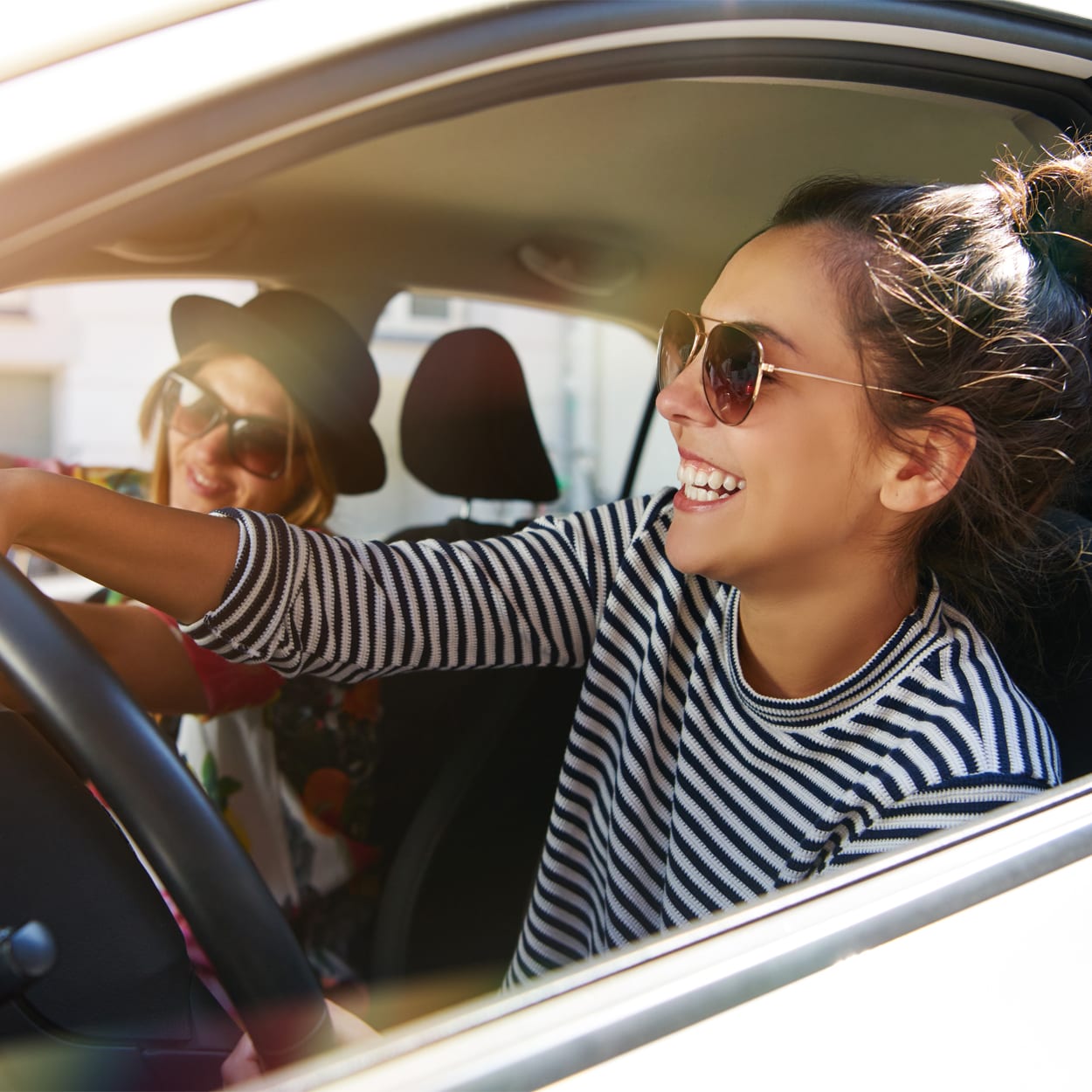 Two laughing young girlfriends driving together in a car