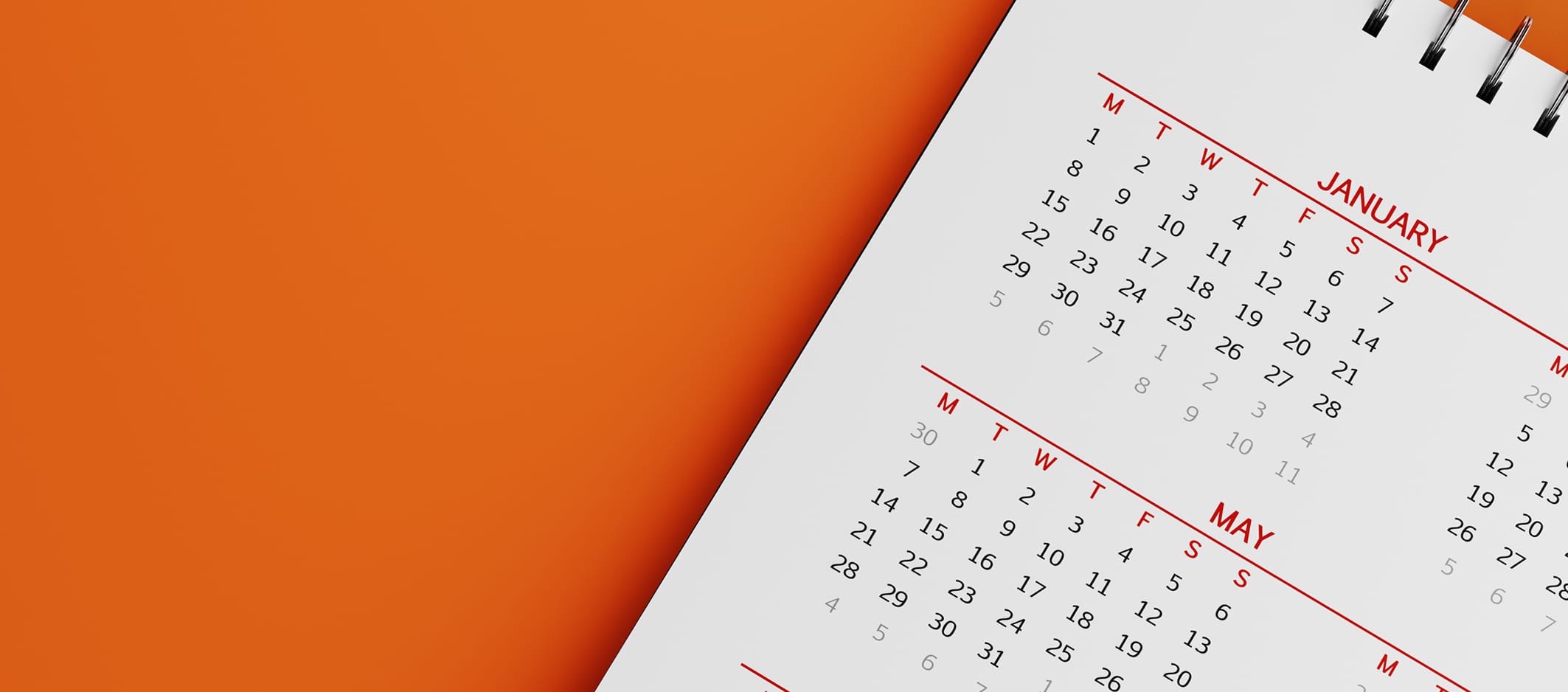 White calendar on orange background. January and may months are visible. Panoramic composition with copy space. Calendar and reminder concept with selective focus.