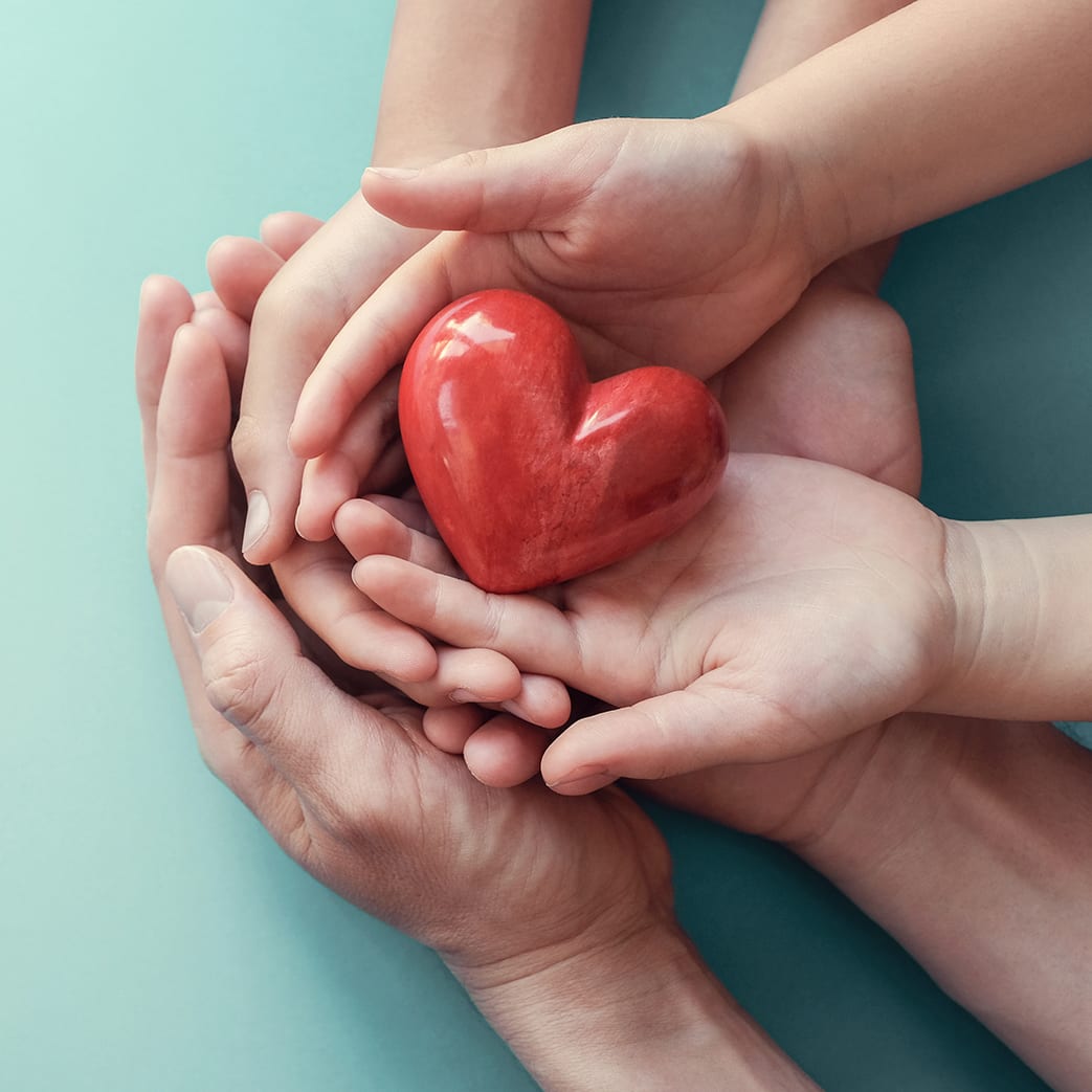 Holding heart in hands Adult and child hands holding a red heart on an aqua background to signify the importance of heart health, donations, CSR concepts, world heart day, world health day, and family day