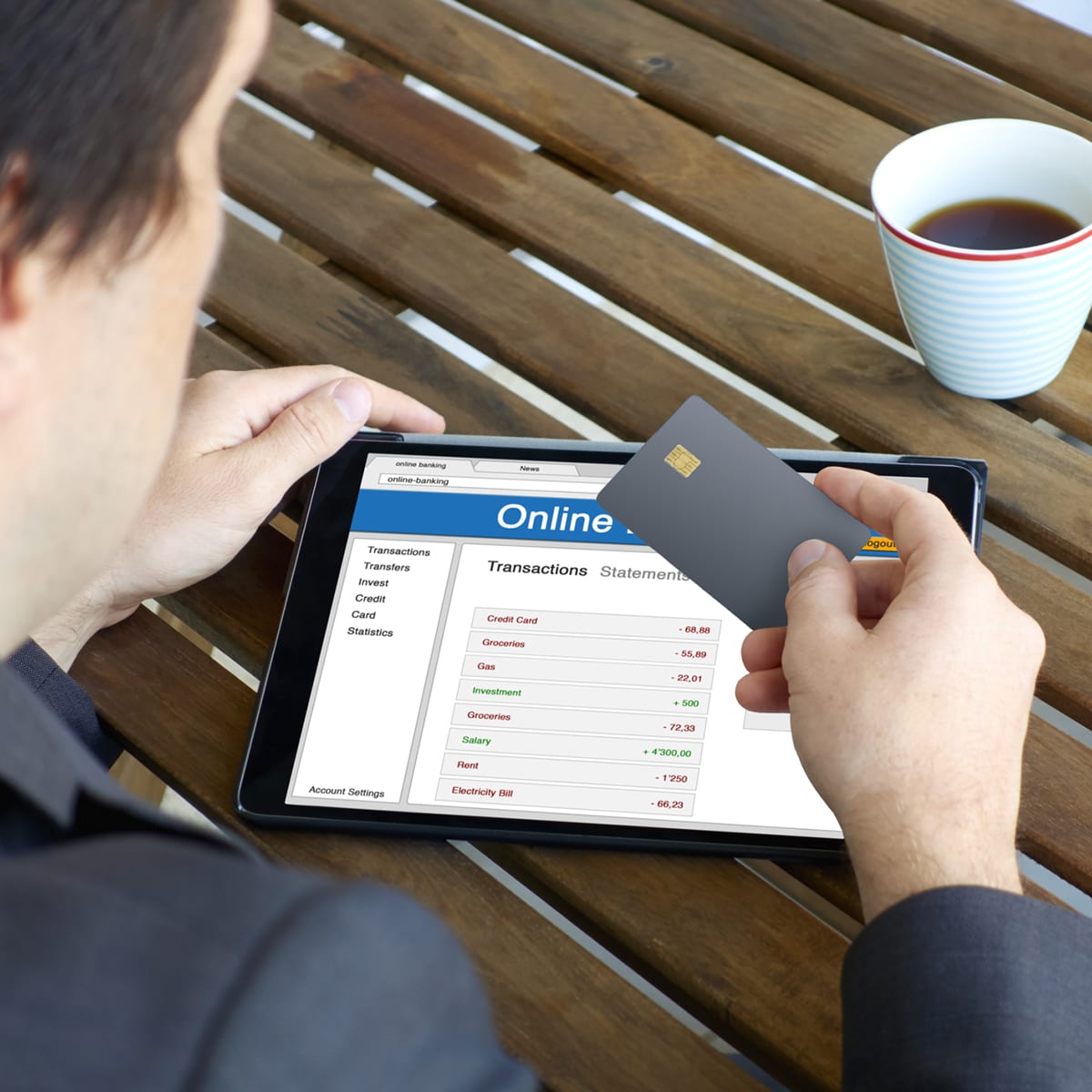 Businessman credit card and tablet computer A businessman using a tablet computer at an outdoor café for online banking. He has a cup of coffee on the table, and a bank card in his hand. The screen displays his banking information with the transactions from his savings and checking accounts.