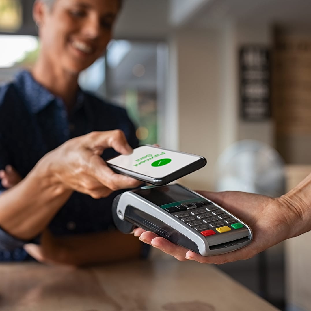 Mature woman paying bill through smartphone using NFC technology in a restaurant. Satisfied customer paying through mobile phone using contactless technology. Close up hands of mobile payment at a coffee shop.