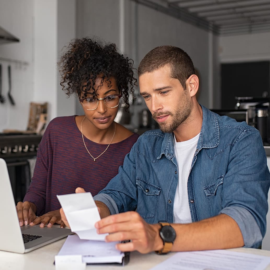 Young multiethnic couple examining home finance couple checking bills while managing accounts on home banking app.
