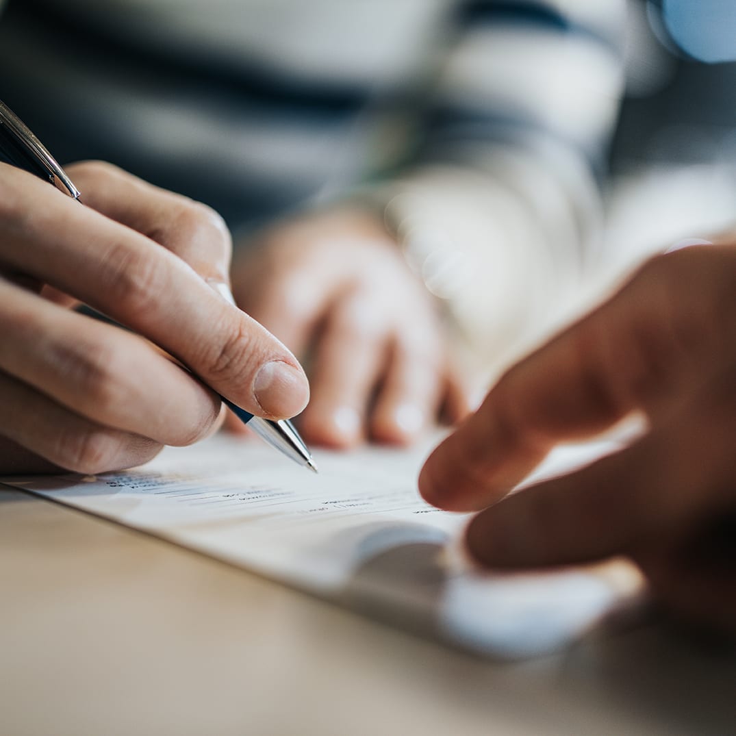 Close up of unrecognizable man signing a contract while financial advisor is aiming at the place he need to sign.