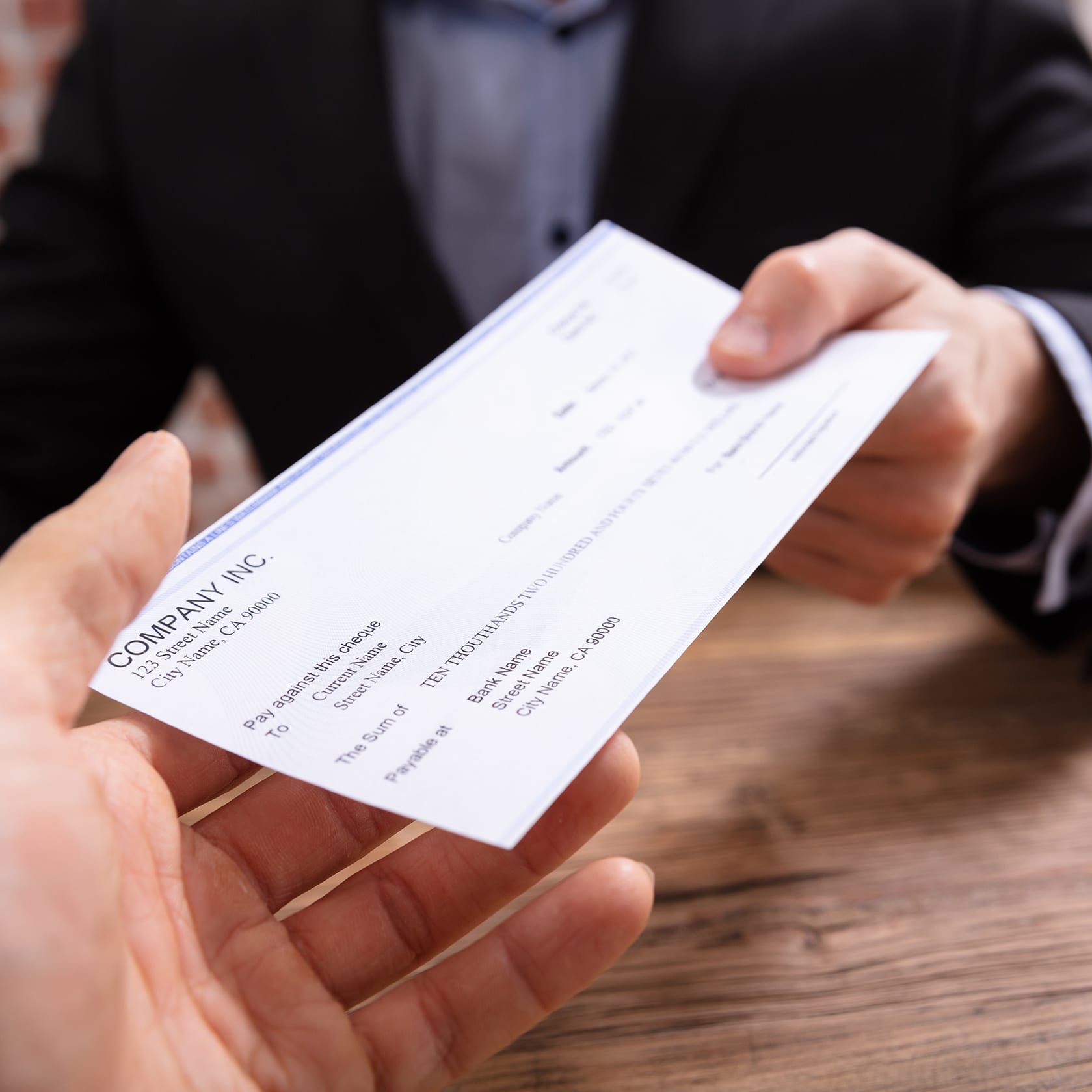 Close-up Of Businessman's Hands Giving Cheque To Other Person In Office