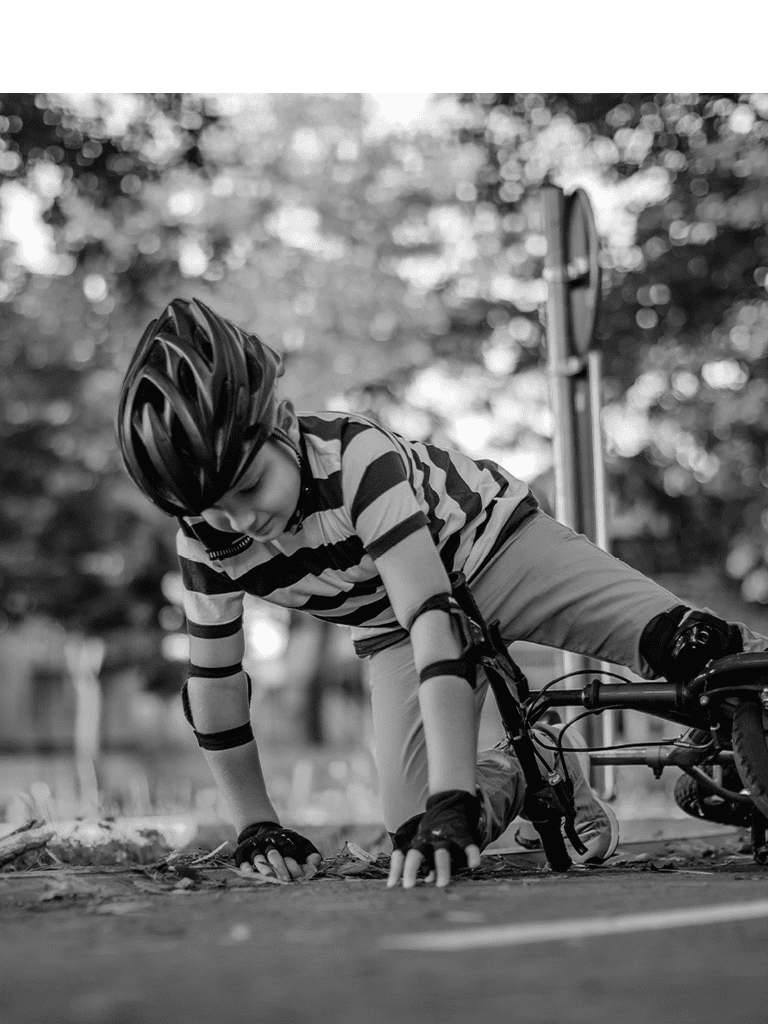 A child wearing a bike helmet and protective pads is picking himself up after a fall