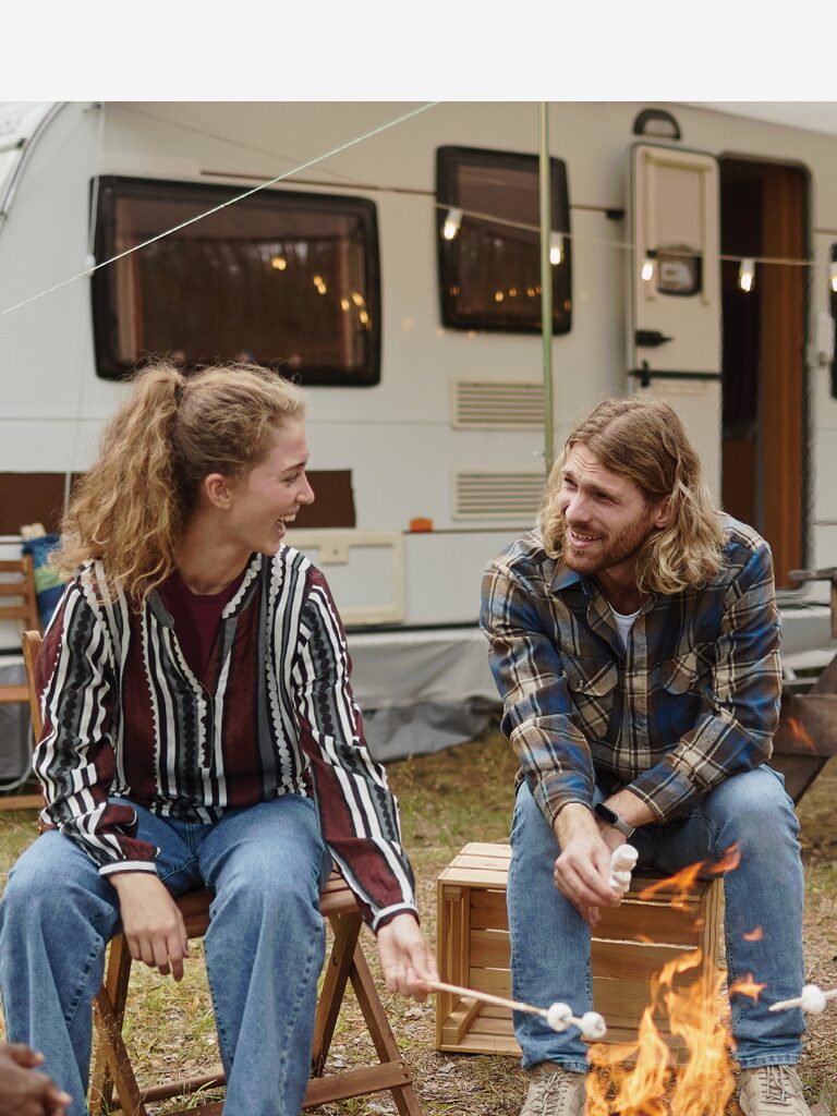 a male and female are sitting on chairs in front of an RV. They are looking at each other and smiling.