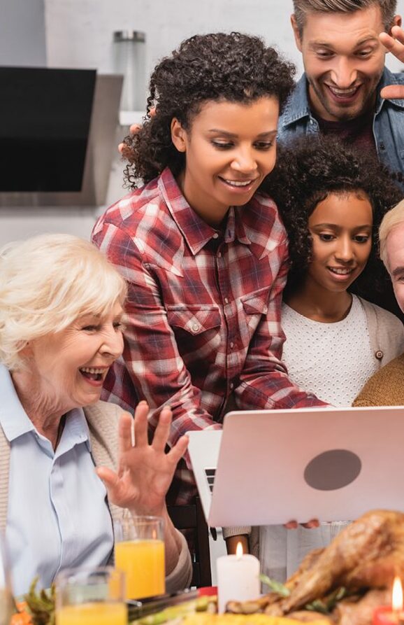 Family members at a dining table facing a laptop screen on a video call on thanksgiving