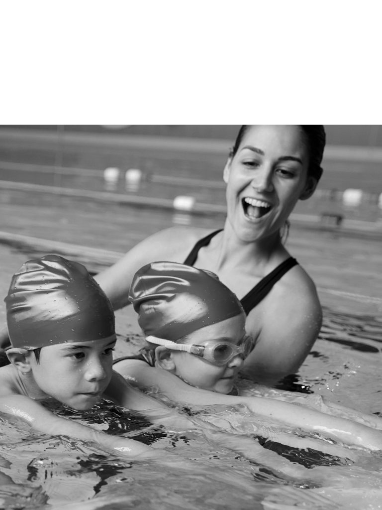 A swim coach helps two young children learn to swim in a pool
