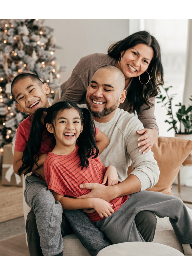 A mom and dad with their two young children pose for a picture together in front of their Christmas tree