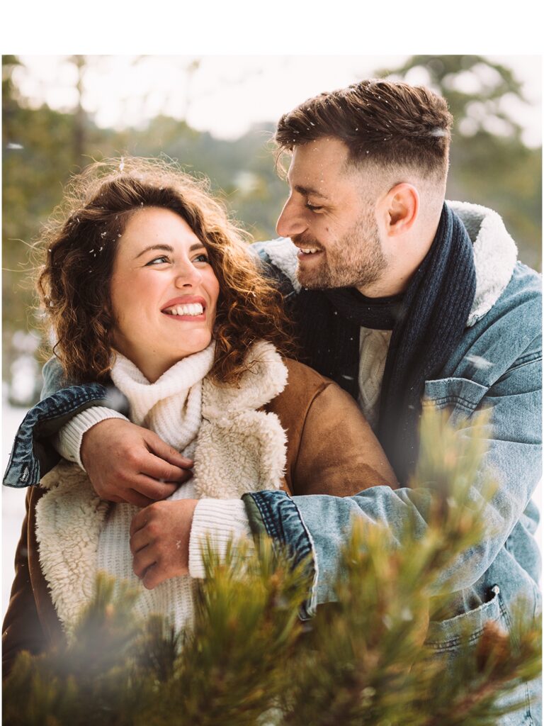 Man and woman are bundled up for the cold weather. He is hugging her and they are smiling.