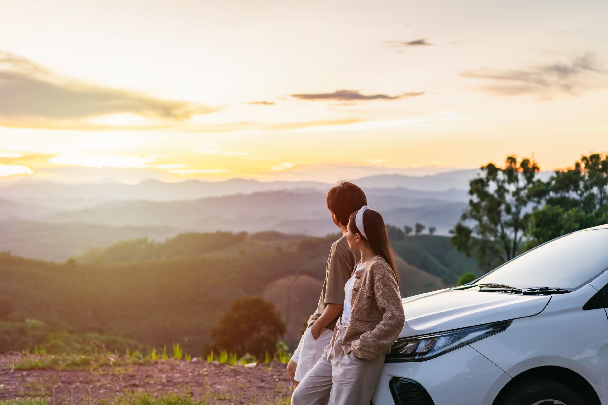 Couple watching the sunset while leaning against their car.