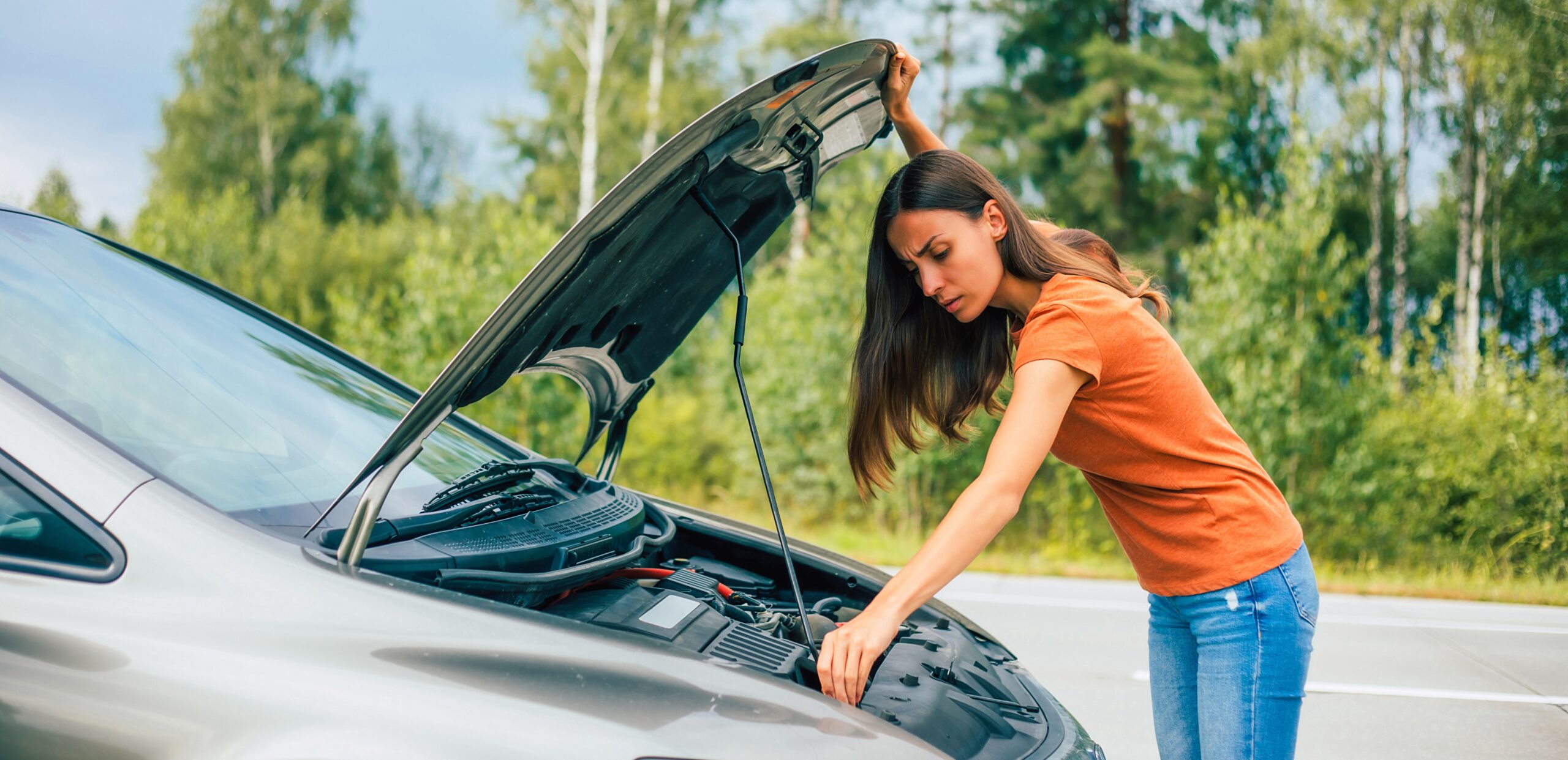 Woman on the side of the road checking under the hood of her car.