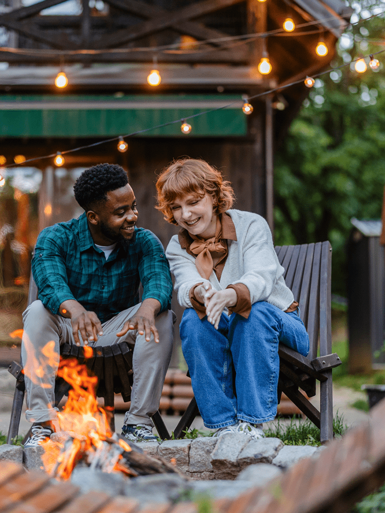 A man and woman are sitting outside their home in lawn chairs, warming by a fire in their fire pit